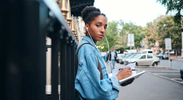 side view serious casual african american student girl denim jacket with notepad confidently looking camera city street