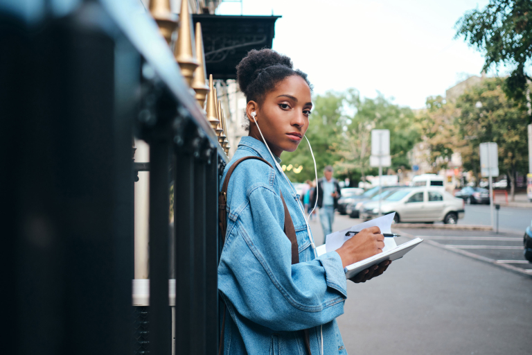 side view serious casual african american student girl denim jacket with notepad confidently looking camera city street